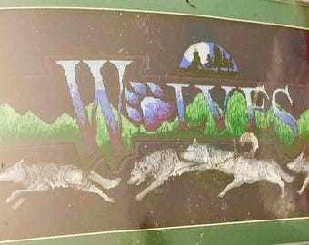 May include: A cross-stitch embroidery depicting a night scene with a full moon and the word "WOLVES" in a stylized font.  Five wolves are running through a forest, with a blue paw print in the center of the word.
