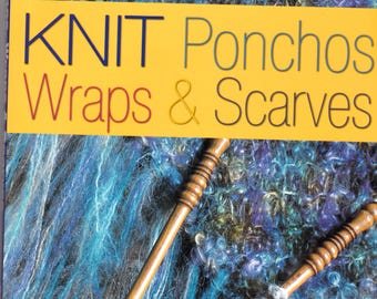 May include: Book cover with the title "KNIT Ponchos Wraps & Scarves" in yellow, red, and black text. The cover features a close-up of a blue and green knitted scarf with wooden knitting needles.
