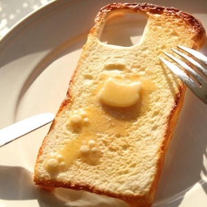 以下が含まれることがあります： 切り抜きの入ったトーストにバターと蜂蜜をかけたもの。フォークとナイフが皿の上にあります。トーストは黄金色で、白い皿の上にあります。