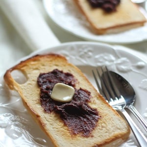 May include: A slice of toasted bread topped with a dollop of red bean paste and a pat of butter. The bread is on a white plate with a fork and spoon.