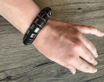 Pulseira rígida gótica incomum, grande, em metal preto, com arcos semicirculares verticais.