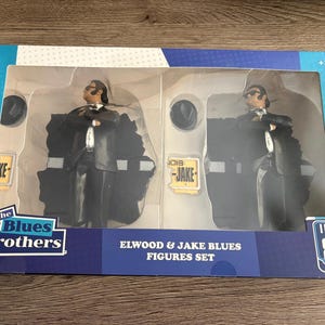 May include: A boxed set of Elwood & Jake Blues figures. The figures are in black suits, white shirts, and sunglasses. The box has a blue and white design with the text "The Blues Brothers" and "I Love the 80's".