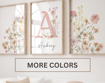 May include: Three framed prints with watercolor floral designs. The center print features a large pink letter "A" with the name "Aubrey" written below. The text "MORE COLORS" is displayed below the prints.