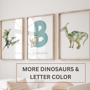 Pu&ograve; includere: Tre stampe incorniciate con illustrazioni ad acquerello di dinosauri. La stampa centrale presenta una lettera B blu e il nome Brandon. La stampa a sinistra mostra uno pterodattilo e la stampa a destra mostra un dinosauro dal collo lungo.