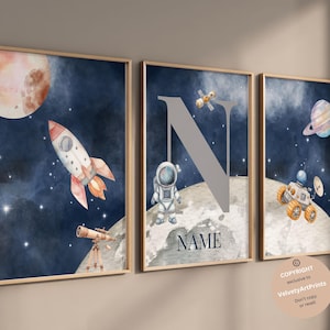 Op de afbeelding: Drie aquarelprints met een ruimtethema. De eerste print toont een raket, een telescoop en een planeet. De tweede print toont een grijze letter N en een astronaut. De derde print toont een ruimteschip en een planeet met ringen. De prints hebben een blauwe achtergrond met witte sterren.