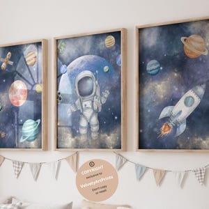 Könnte beinhalten: Drei gerahmte Aquarelldrucke, die eine Weltraumszene mit einem Astronauten, Planeten und einer Rakete darstellen. Der Astronaut schwebt im Weltraum, umgeben von Sternen und Planeten. Die Rakete fliegt durch den Weltraum und hinterlässt eine Rauchspur. Die Drucke sind vor einer weißen Wand mit einer darunter hängenden Flaggenkette platziert.
