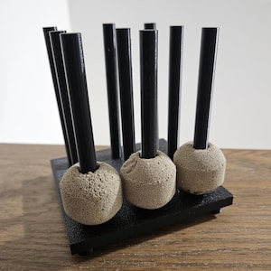 May include: A black stand with eight black rods and beige foam balls on the ends. The stand is on a wooden surface.