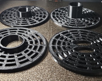 May include: Four black 3D printed circular coasters with a geometric design and a center hole. The coasters are on a gray surface.