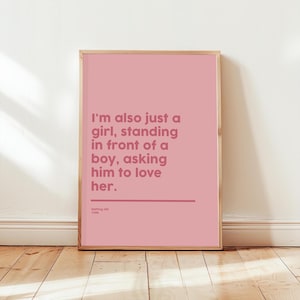 Op de afbeelding: Een roze ingelijste print met de tekst: "I'm also just a girl, standing in front of a boy, asking him to love her." De print bevat ook de tekst "Notting Hill 1999". De lijst heeft een lichte houtkleur.
