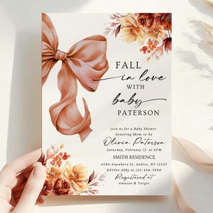 May include: Baby shower invitation featuring a peach bow and floral decorations. The text reads "Fall in love with baby Paterson" and includes event details. The invitation is held by a hand.