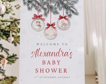 May include: A white baby shower welcome sign on a wooden easel. The sign features the text "Welcome to Alexandra's Baby Shower" in red script, with the date "12th of December, Saturday" below. The top of the sign has illustrations of Christmas ornaments.