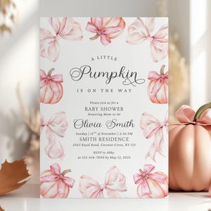 May include: A rectangular baby shower invitation card featuring a white background with watercolor illustrations of light pink pumpkins and bows. The text reads: A little Pumpkin is on the way, Please join us for a BABY SHOWER, Olivia Smith, Sunday, 15th of November, 2:30 PM, SMITH RESIDENCE, 2563 Royal Road, Coconut Grove, NY 125, RSVP to Abby at 123-456-7890 by May 12, 2025.