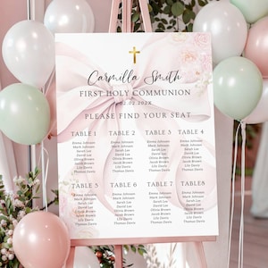 May include: A First Holy Communion seating chart on an easel, decorated with pastel balloons and floral accents. The sign features the name "Carmilla Smith" and the date, with a cross symbol at the top. Tables are listed with guest names.