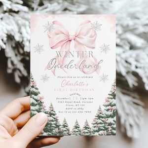 May include: A rectangular invitation with a winter theme. The invitation features a pink bow, snowflakes, and text that reads "Winter Onederland" and "Charlotte's First Birthday." The bottom of the invitation has a row of snow-covered trees.