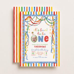 Puede incluir: Una tarjeta de invitación para el primer cumpleaños con un borde de rayas coloridas, serpentinas colgantes y la foto de un bebé con un gorro de fiesta. El texto dice: it's fun to be ONE, THEODORE, first birthday, March 10, 123 Little Peanut Road Chicago, 8 PM.