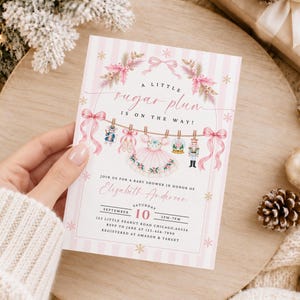 May include: A baby shower invitation card with a pink and white striped background. It features a watercolor illustration of a tutu, ballet slippers, a nutcracker, and a mouse hanging on a string with pink bows. Text reads: A LITTLE sugar plum IS ON THE WAY! JOIN US FOR A BABY SHOWER IN HONOR OF Elizabeth Anderson SATURDAY SEPTEMBER 10 2PM-7PM 123 LITTLE PEANUT ROAD CHICAGO, 60556 RSVP TO JANE AT 123-456-7890 REGISTERED AT AMAZON & TARGET.