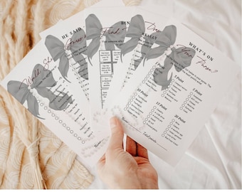 May include: A stack of bridal shower game cards with gray bow and pearl accents. The games include "Would She," "He Said," "Find," and "What's on Your Purse?" The text "21 Black Bow & Pearls Bridal Shower Games" is at the bottom.