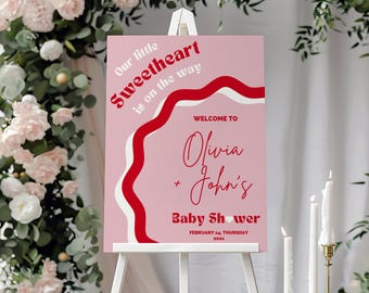 May include: Pink and red baby shower welcome sign with the text "Our little Sweetheart is on the way" and "Welcome to Olivia + John's Baby Shower" with the date "February 14, Thursday 202x".