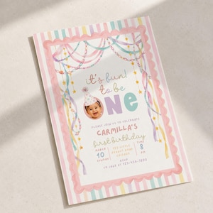 May include: A rectangular first birthday invitation card featuring a pastel striped border and a scalloped pink frame. The design includes watercolour-style hanging garlands, stars, and the text it's fun to be one with a photo of a baby in a party hat.