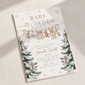 Op de afbeelding: Een uitnodigingskaart voor een babyshower met de tekst Baby It's Cold Outside, een waslijn met winterse babykleding en twee besneeuwde dennenbomen met beige strikken. De kaart bevat de evenementgegevens voor Amanda Smith op 14 december.