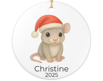 May include: A round, white Christmas ornament featuring a watercolor illustration of a gray mouse wearing a red Santa hat. The text "Christine 2025" is printed in black below the mouse. A gold string is attached for hanging.