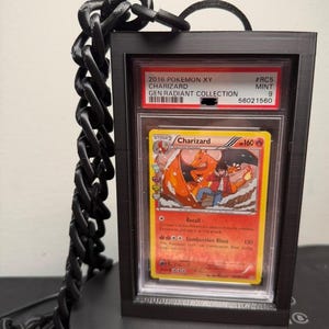 Peut inclure: Un pr&eacute;sentoir noir avec une cha&icirc;ne pour une carte Pok&eacute;mon Charizard. La carte provient de la collection 2016 Pokemon XY Generations Radiant. La carte est not&eacute;e Mint 9.