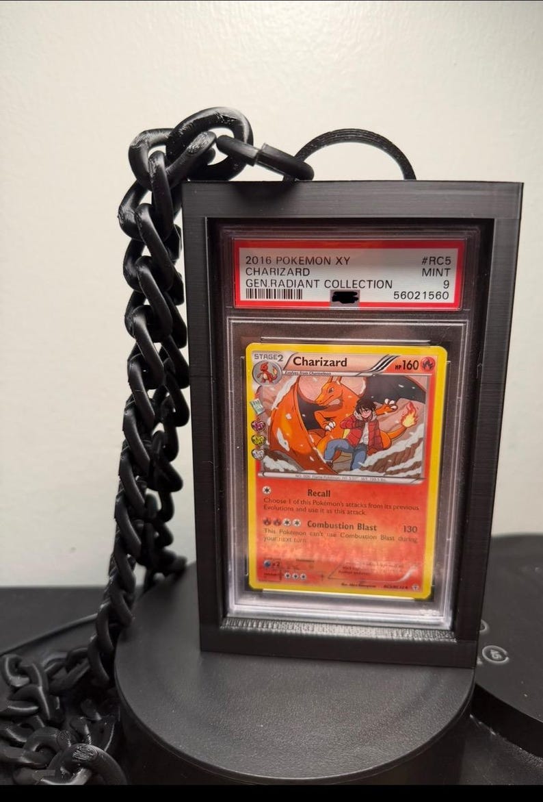 Peut inclure: Un pr&eacute;sentoir noir avec une cha&icirc;ne pour une carte Pok&eacute;mon Charizard. La carte provient de la collection 2016 Pokemon XY Generations Radiant. La carte est not&eacute;e Mint 9.