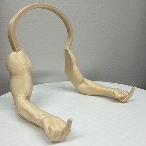 May include: A beige-colored, 3D-printed sculpture of two arms and a curved structure. The arms are extended, with one hand making a gesture. The sculpture is on a white surface.