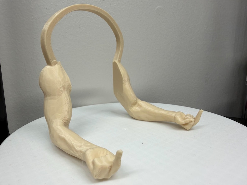 May include: A beige-colored, 3D-printed sculpture of two arms and a curved structure. The arms are extended, with one hand making a gesture. The sculpture is on a white surface.