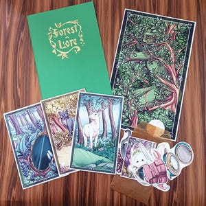 May include: A collection of art prints and stickers featuring forest-themed illustrations. Includes a green journal with gold lettering that reads "Forest Liore". The prints depict scenes with deer, cats, and mirrors in a forest setting.