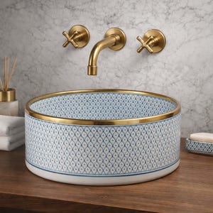 Può includere: Un lavabo rotondo in ceramica con un motivo geometrico blu e bianco e un bordo dorato. Rubinetteria dorata. Il lavabo è su una superficie di legno. Il diametro del lavabo è di circa 40 cm.