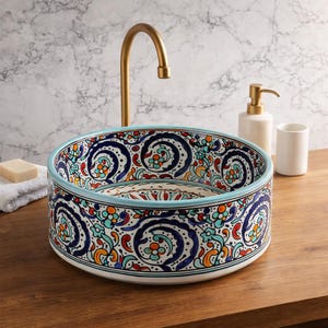 Puede incluir: Un lavabo de cerámica decorativo con un patrón vibrante e intrincado en azul, naranja y verde. El lavabo tiene un borde azul claro y está sobre una superficie de madera. Un grifo y accesorios dorados son visibles en el fondo.
