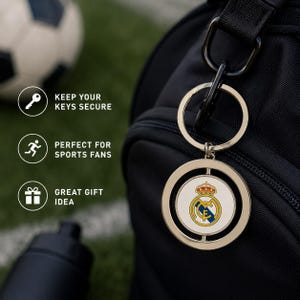 May include: A silver keyring with a circular pendant displaying the Real Madrid team logo. The keyring is attached to a black bag. Text on the left reads: "KEEP YOUR KEYS SECURE", "GREAT GIFT IDEA".