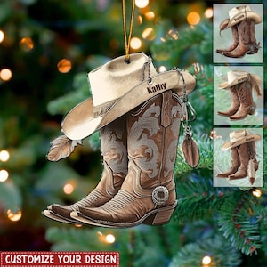 Puede incluir: Adorno de bota y sombrero de vaquero marrón con el nombre "Kathy" en el sombrero. El adorno tiene una pluma y una hebilla plateada decorativa. El fondo es un árbol de Navidad con una pancarta "Customize Your Design".
