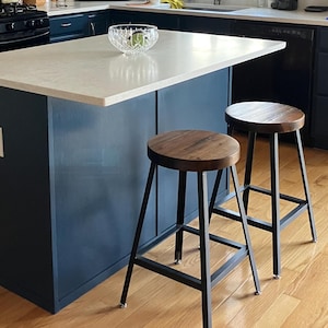 May include: A kitchen with navy blue cabinets, a white countertop island, and wooden stools. The walls are painted a deep red. The kitchen has a stainless steel range hood, a microwave, and a window with blinds.