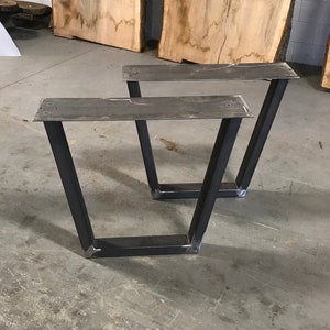 May include: Two black metal table legs with a rectangular top. The legs are angled and have a welded construction.