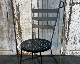 May include: Black metal chair with a round, perforated seat and a curved back. The chair is standing on a concrete floor.