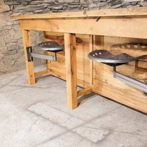 May include: A rustic wooden table with two metal industrial-style swivel seats attached to the underside. The table is made of reclaimed wood and has a natural finish. The seats are made of metal and have a black finish.