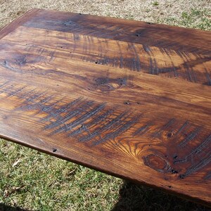 May include: Close-up of a rustic wooden table top with a dark brown stain. The wood grain is visible and there are several knots and imperfections in the surface.