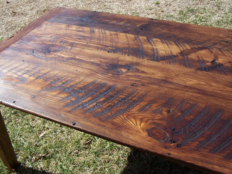 May include: Close-up of a rustic wooden table top with a dark brown stain. The wood grain is visible and there are several knots and imperfections in the surface.