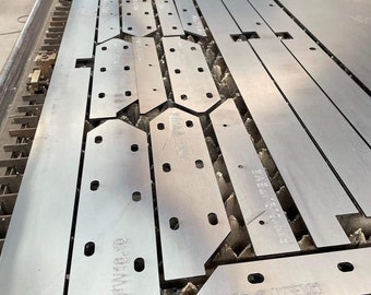 May include: A close-up of several metal plates with holes and markings. The plates are arranged in rows on a textured surface. The plates are labeled with the text "FWIG & ITEM" and "FWIG & ITEM 2".