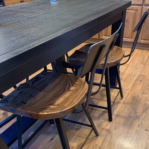 Op de afbeelding: Drie zwarte metalen en houten barstoelen met een zwarte tafel op de achtergrond. De krukken hebben een donkerhouten zitting en zwarte metalen poten.