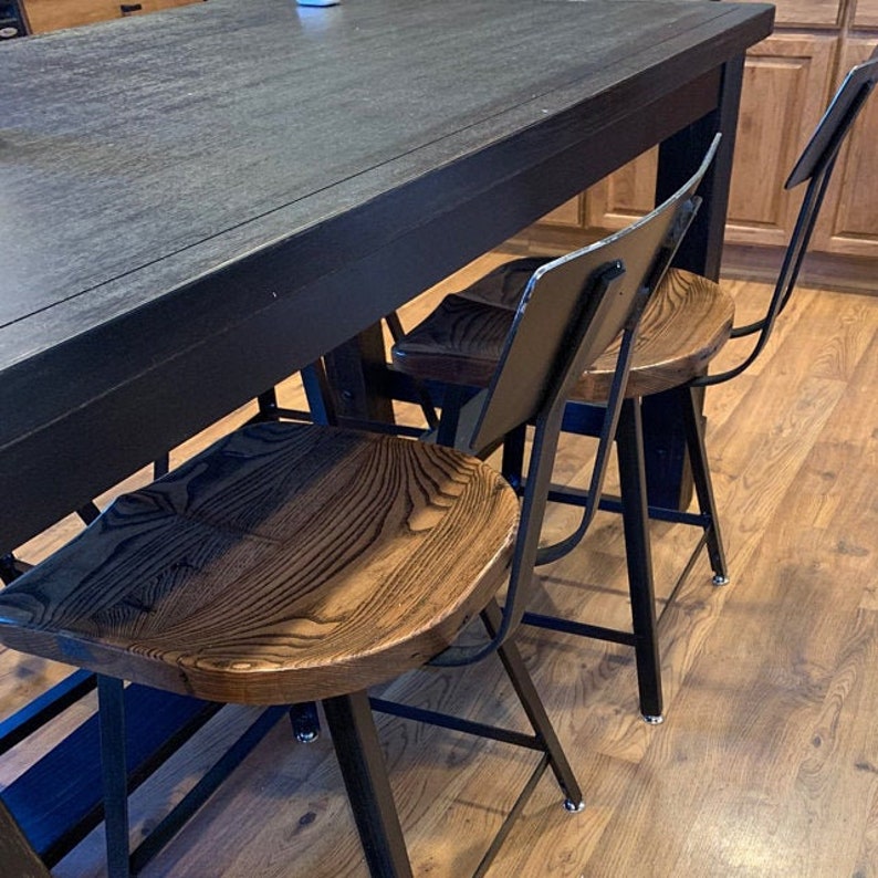 Op de afbeelding: Drie zwarte metalen en houten barstoelen met een zwarte tafel op de achtergrond. De krukken hebben een donkerhouten zitting en zwarte metalen poten.
