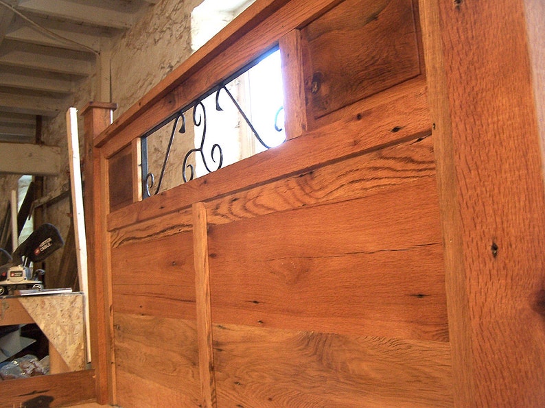 Op de afbeelding: Een houten hoofdbord met een decoratief metalen ontwerp in het midden. Het hoofdbord is gemaakt van gerecycled hout en heeft een rustieke uitstraling.