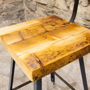 May include: A wooden bar stool with a reclaimed wood seat and black metal legs. The seat is made of multiple pieces of wood that have been joined together.