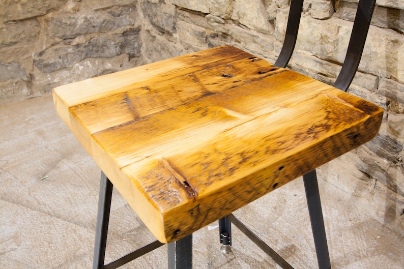 May include: A wooden bar stool with a reclaimed wood seat and black metal legs. The seat is made of multiple pieces of wood that have been joined together.