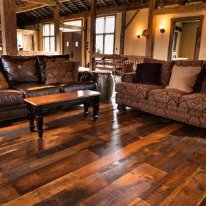 May include: A rustic living room with hardwood floors, two sofas, and a wooden coffee table. One sofa is brown leather, the other is patterned. Decorative pillows in various colors and patterns add to the cozy atmosphere.
