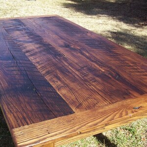 May include: A rustic wooden table with a dark brown stain. The table top is made of reclaimed wood planks with visible knots and grain patterns. The table has a simple, rectangular design with a slightly distressed finish.