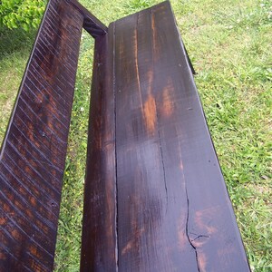 May include: A dark brown wooden bench with a slatted back and a smooth, polished seat. The bench is made of reclaimed wood and has a rustic, farmhouse style.