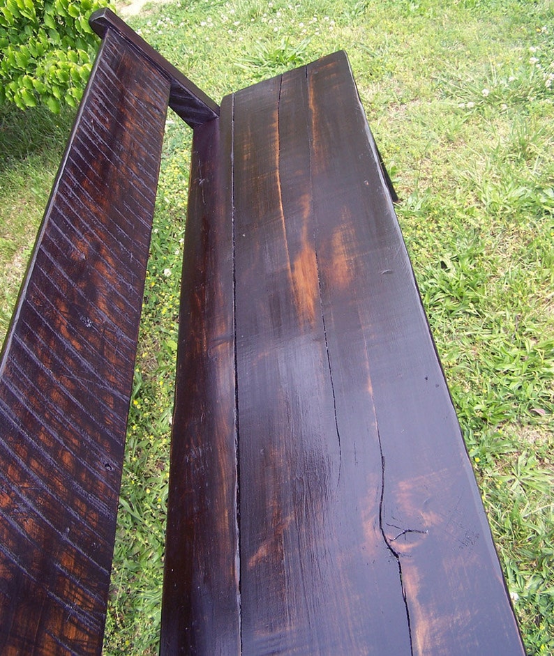 May include: A dark brown wooden bench with a slatted back and a smooth, polished seat. The bench is made of reclaimed wood and has a rustic, farmhouse style.